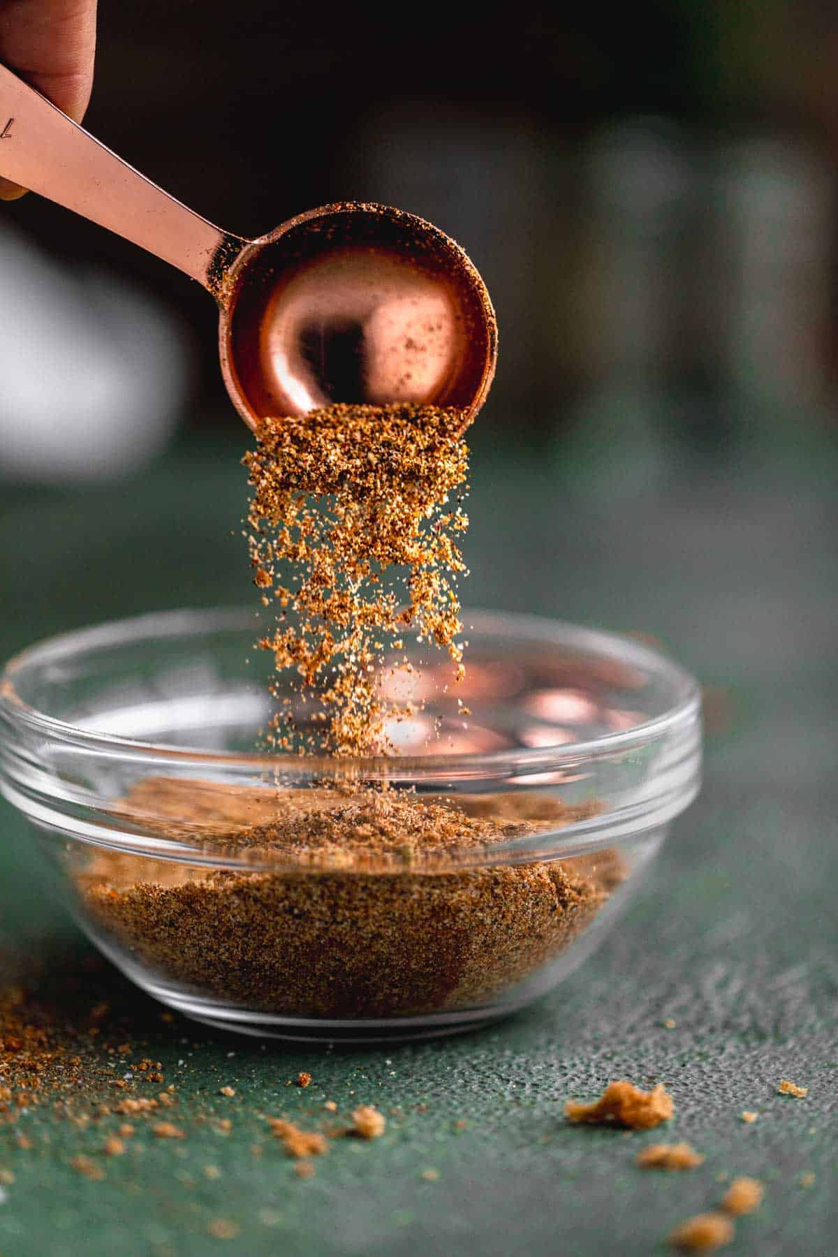 Chicken taco seasoning being poured out of a tablespoon into a small dish.