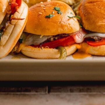 A tray full of Philly cheesesteak sliders with one tipped to the side.