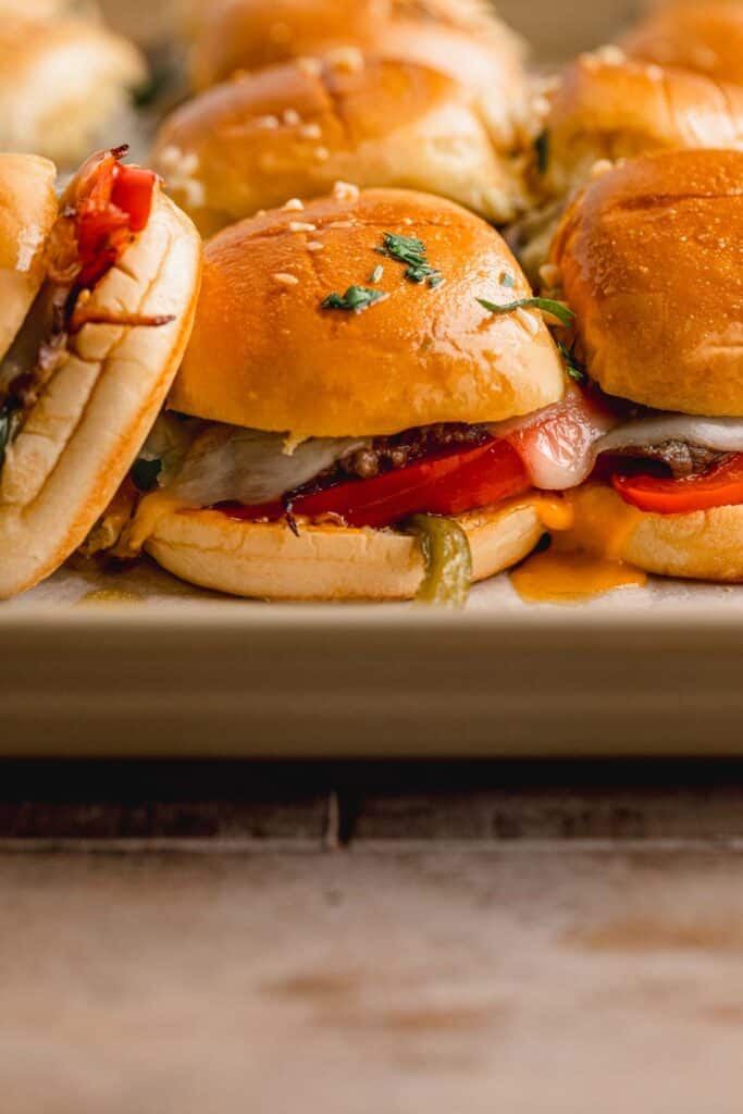 A tray full of Philly cheesesteak sliders with one tipped to the side.