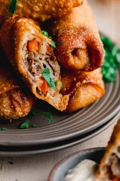 Philly cheesesteak egg rolls stacked on a plate.