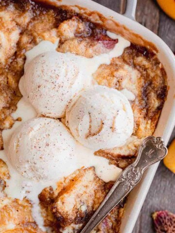 Peach Cobbler recipe with cake mix in a baking dish topped with scoops of vanilla ice cream.