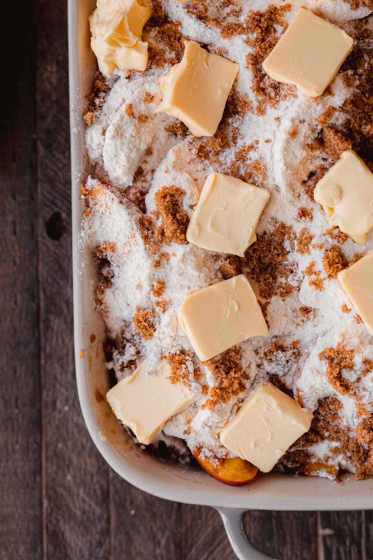Peaches topped with boxed cake mix and pats of butter in a baking dish. 