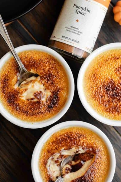 Pumpkin creme brulee with cracked sugar tops and pumpkin spice bottle next to it.