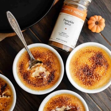 Pumpkin creme brulee in ramekins with spoons and pumpkin spice next to them.