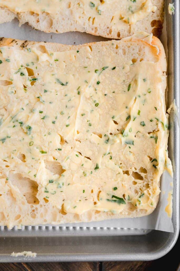 Roasted garlic butter spread over focaccia bread on a sheet pan.