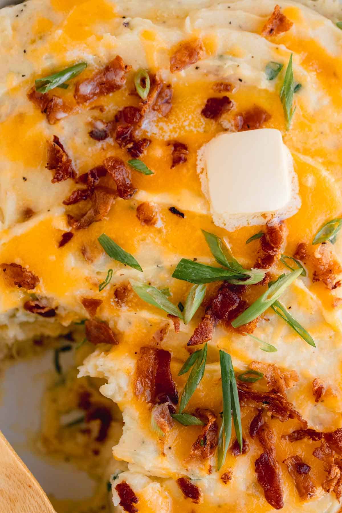 Loaded Potato Casserole in a baking dish with bacon, green onions and butter on top.