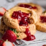 A stack of Strawberry Cheesecake Cookies with strawberry compote dripping down from a bite taken out of the top cookie.