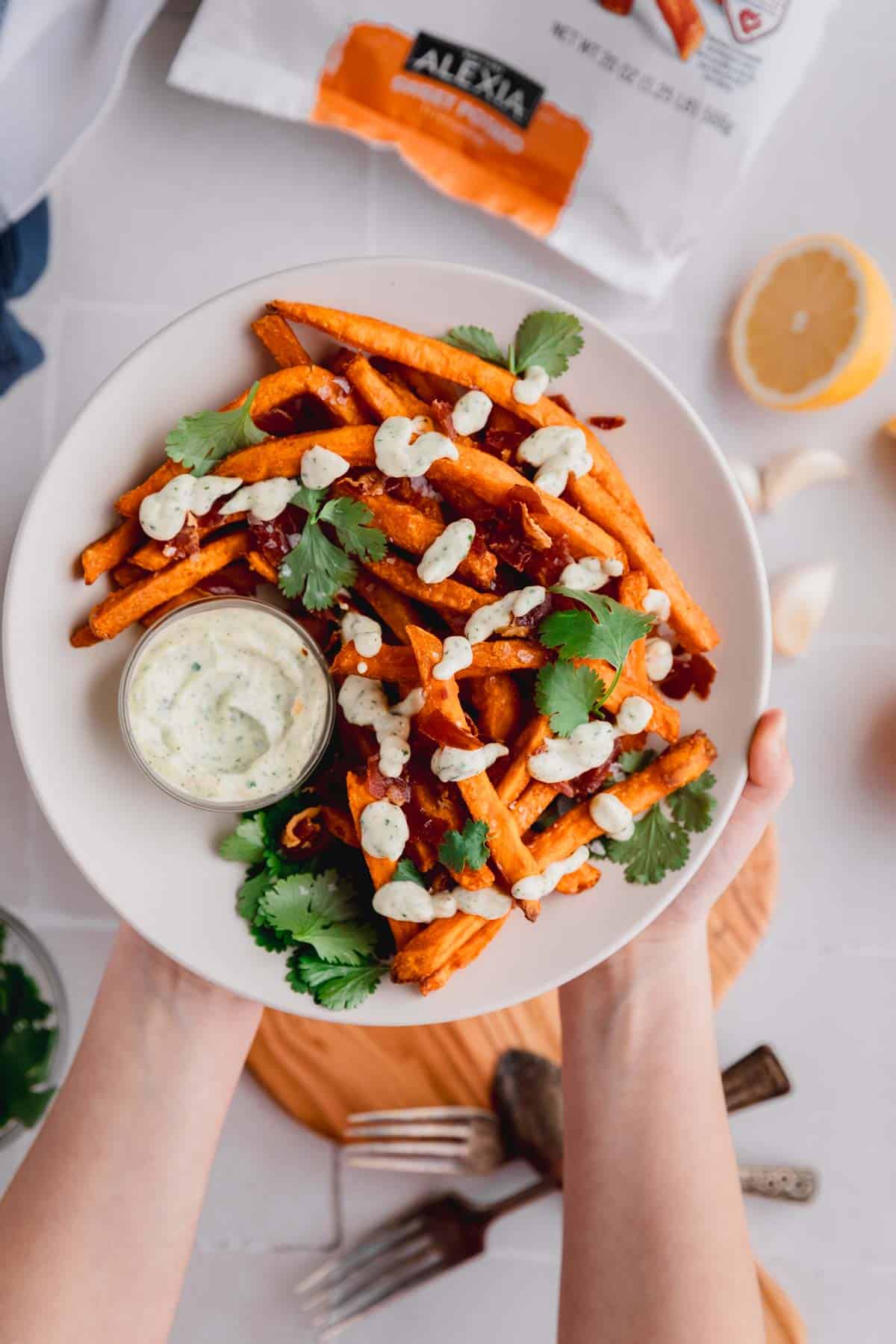 A plate of sweet potato fries made in the air fryer topped with cilantro and sauce. 