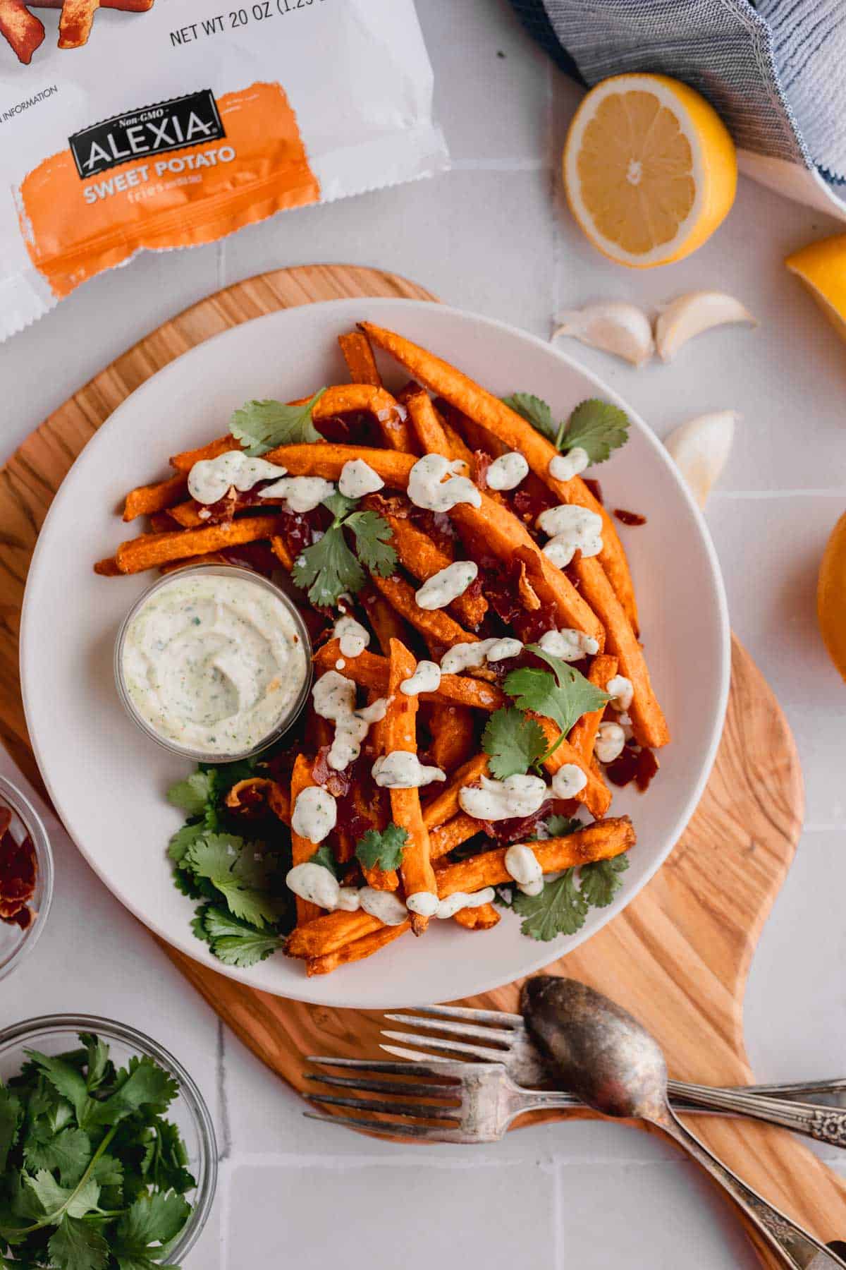 Alexia Sweet Potato Fries in the air fryer topped with cilantro aioli and crispy prosciutto on a plate, topped with fresh cilantro leaves. 