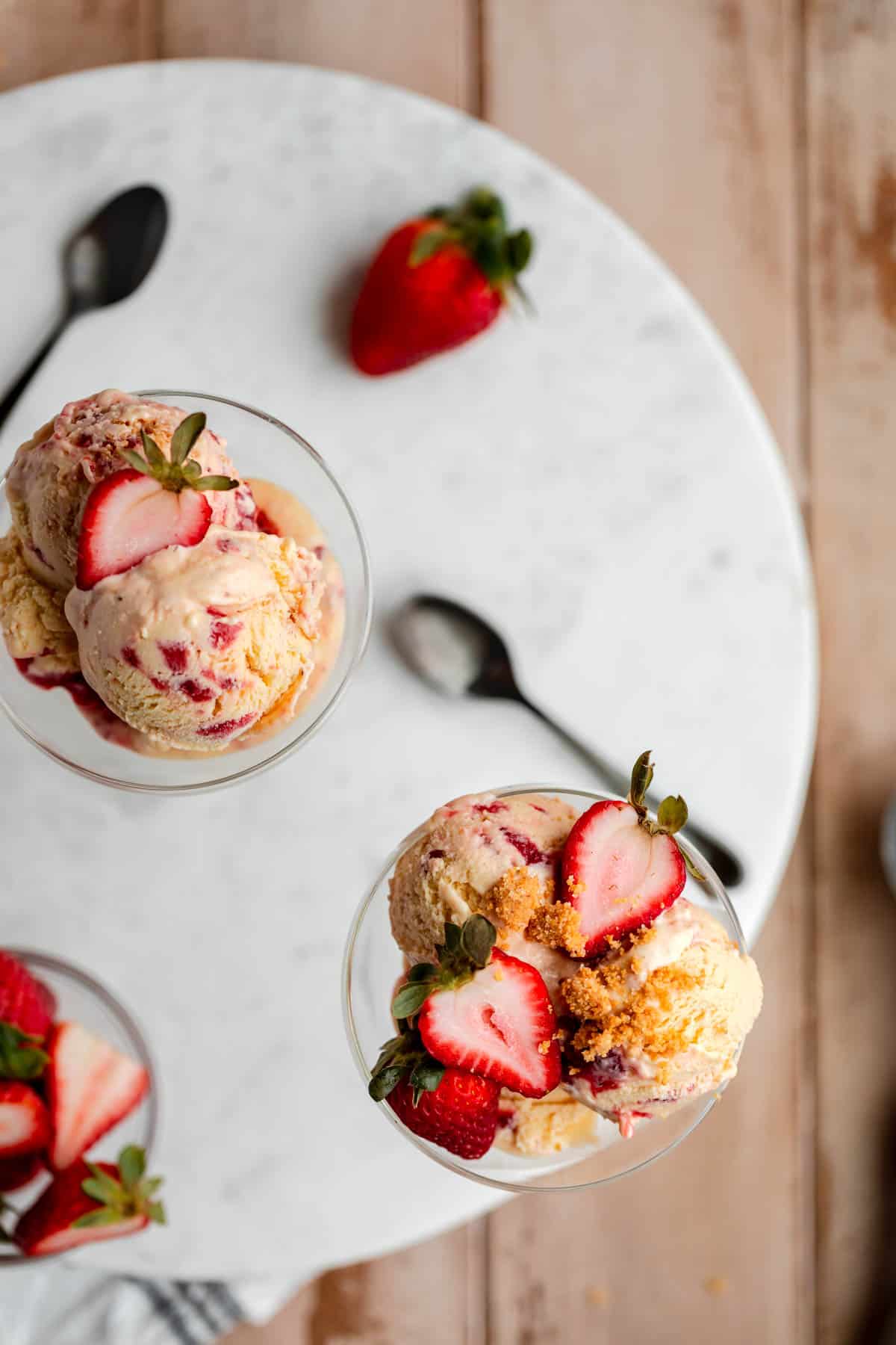 Strawberry Cheesecake Ice Cream served into two cocktail glasses topped with strawberries and buttered graham cracker crumbs. 