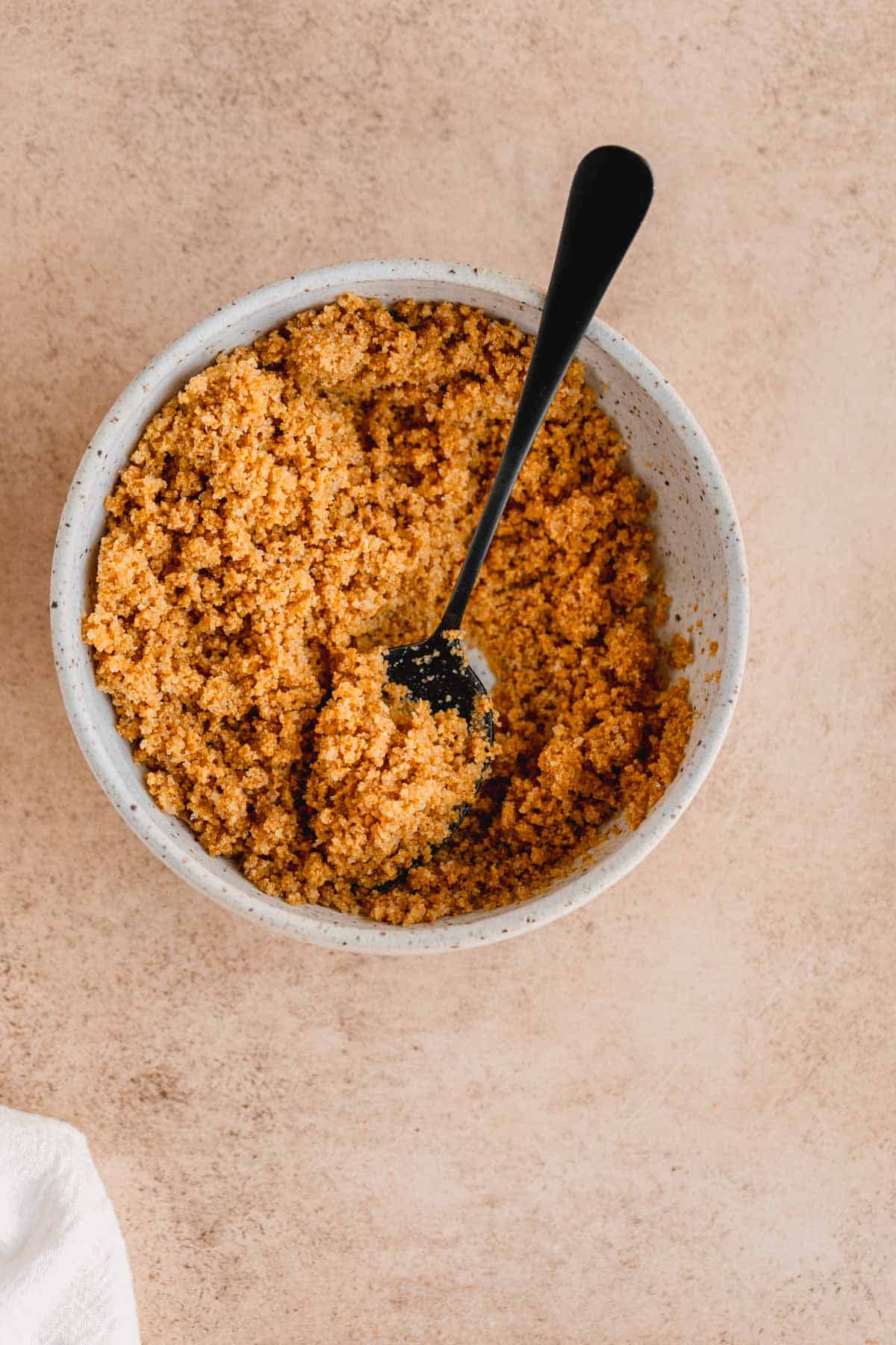 Buttered graham cracker crumbs in a bowl with a spoon. 