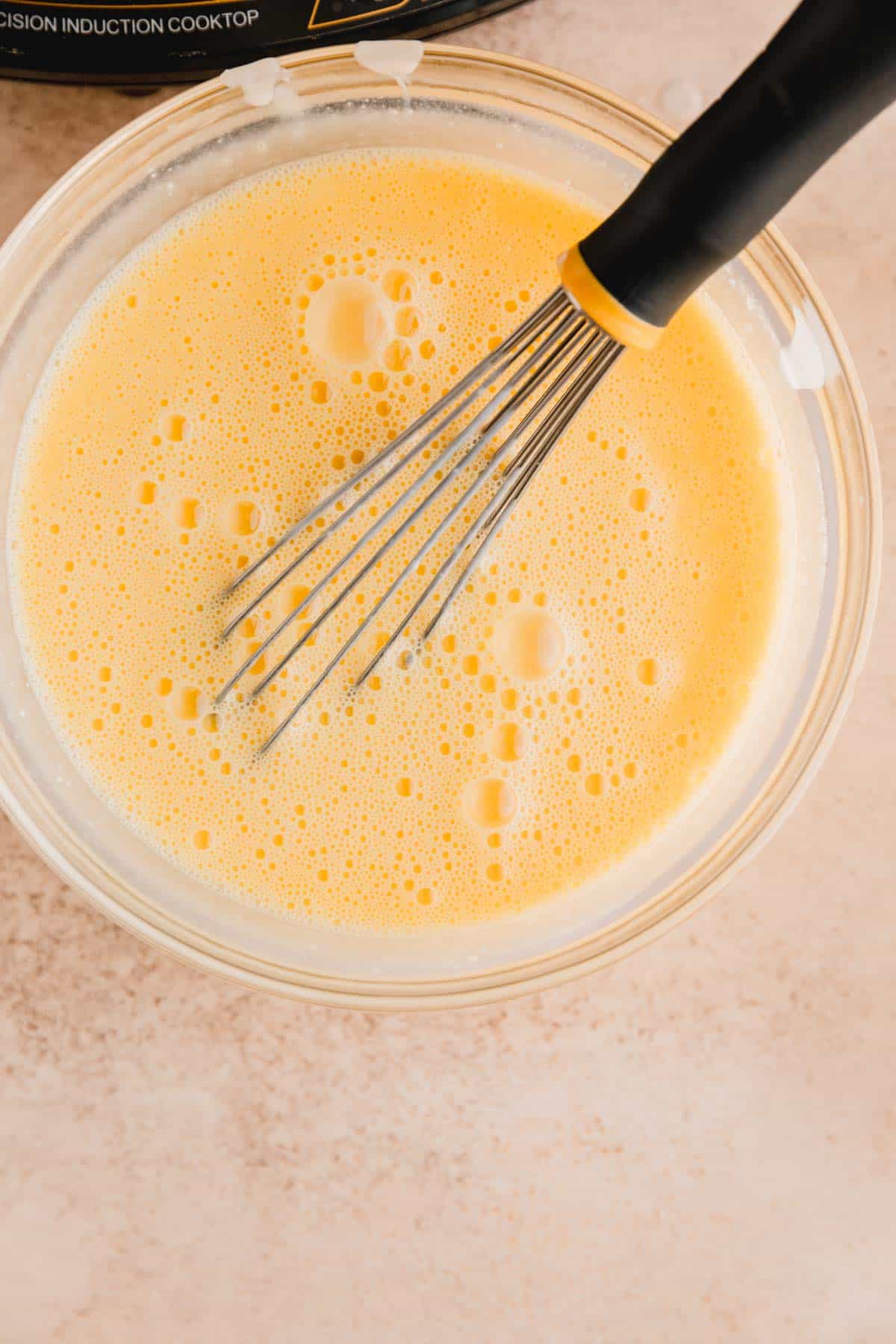 Warm cream mixture being whisked into the egg yolks.