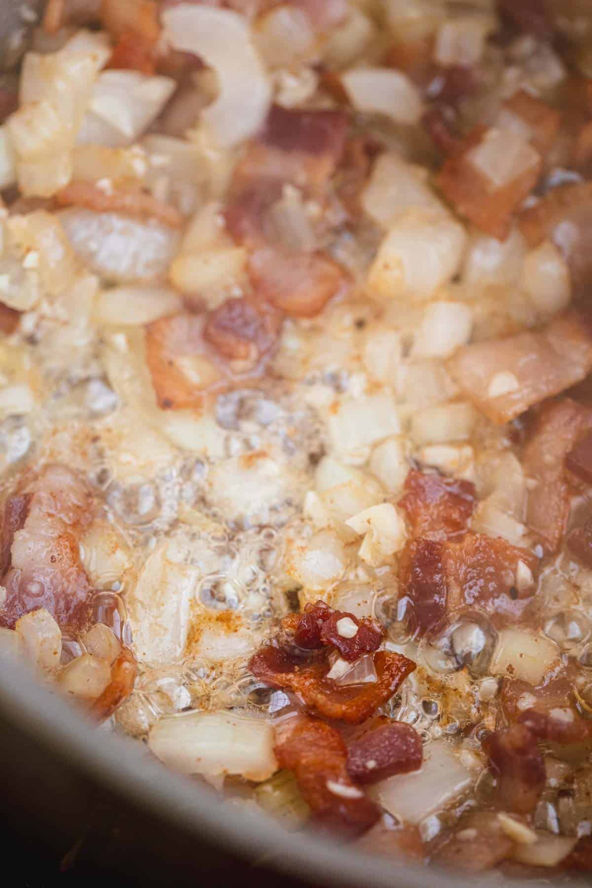 Garlic on top of cooked bacon and onions in a pot.