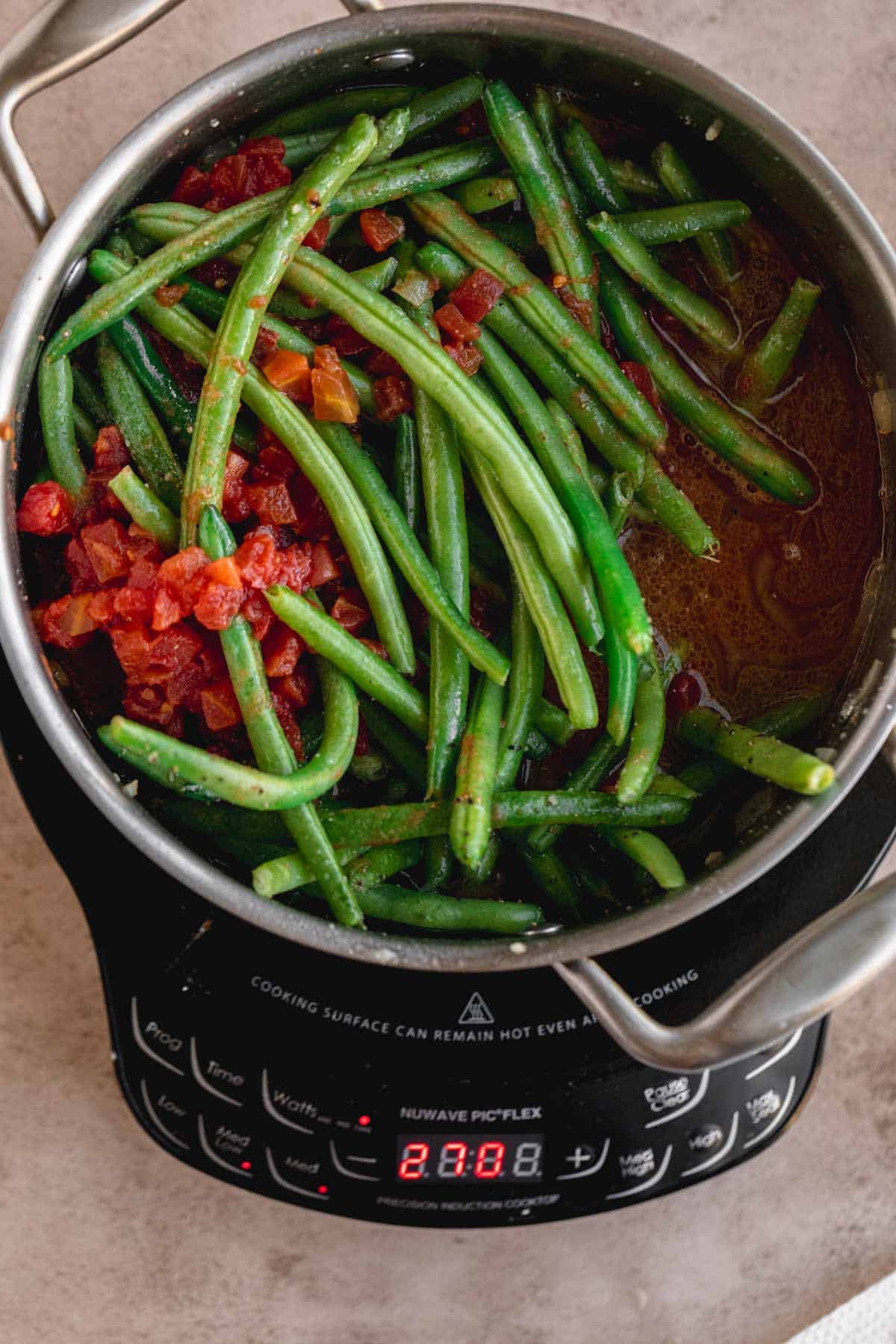 Green beans with bacon, onion, tomato, garlic, seasoning and chicken broth in a pot. 