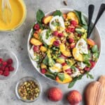 Summer Peach Burrata Salad with raspberries, fresh herbs, arugula and honey mustard dressing in a salad bowl with peaches, pistachios, raspberries and dressing on the side.