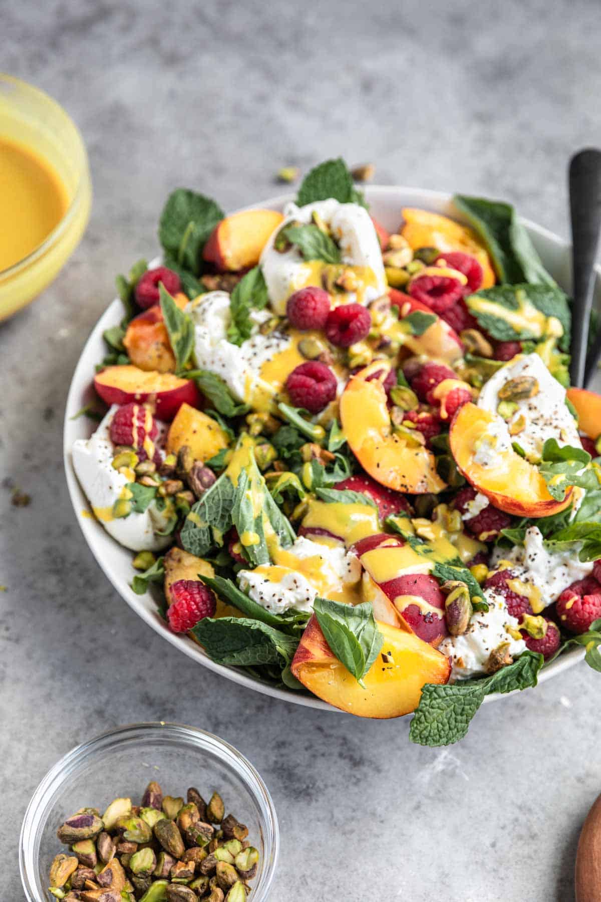 Peach Burrata Salad ingredients tossed together in a bowl, topped with honey mustard dressing. 