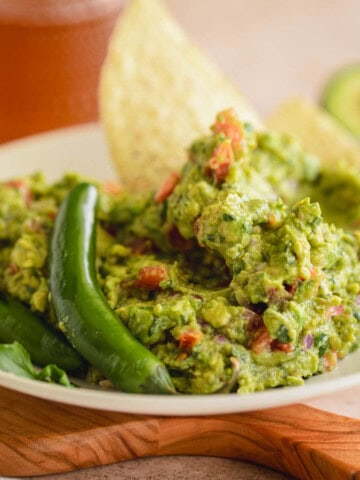 Spicy Guacamole recipe in a bowl with serrano peppers and tortilla chips.