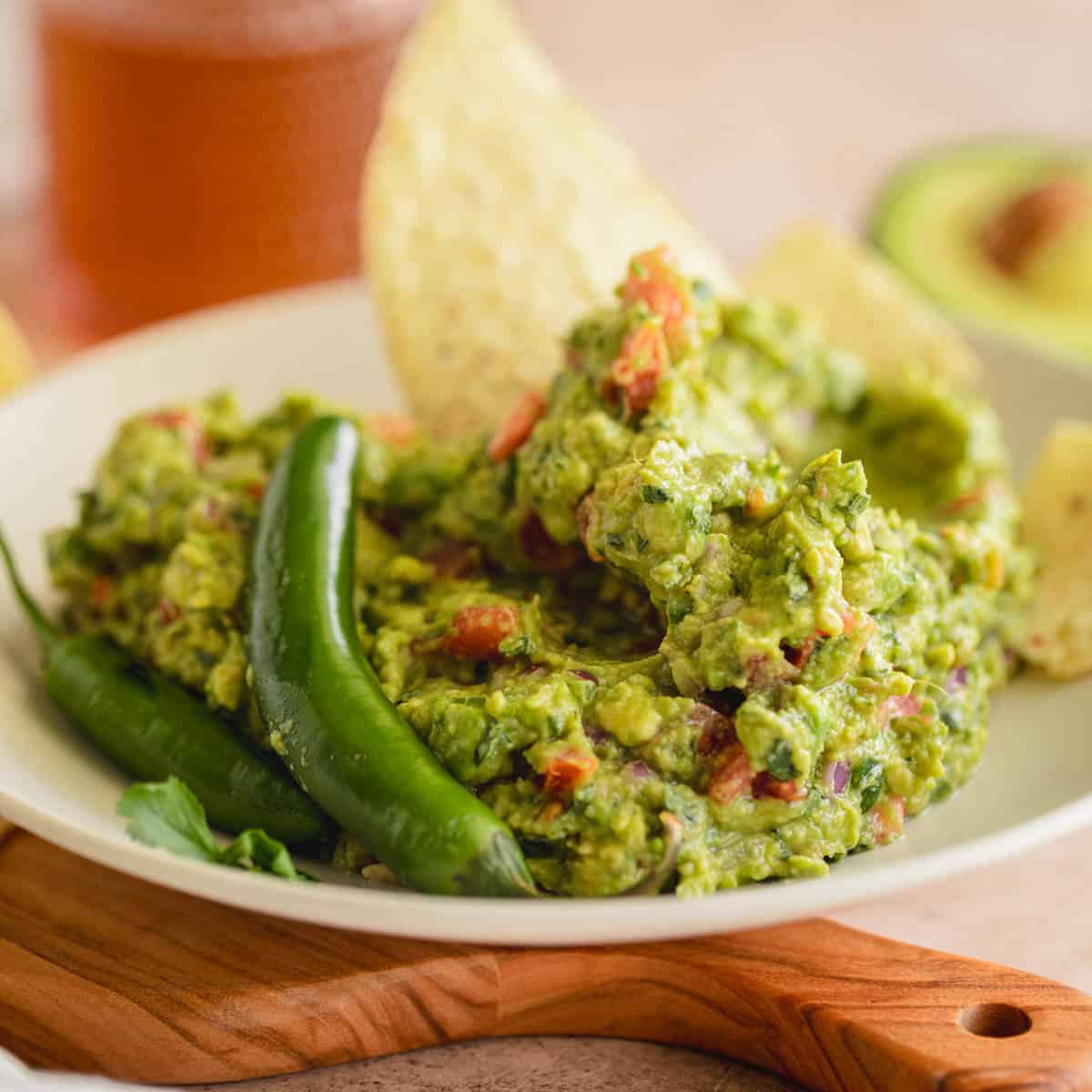 Spicy Guacamole recipe in a bowl with serrano peppers and tortilla chips.