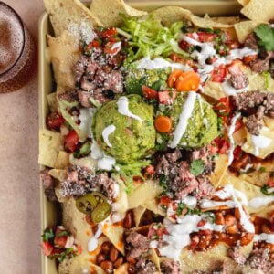 Loaded Steak Nachos recipe topped with sour cream, salsa, guacamole and jalapenos.