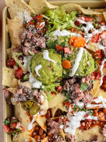 Loaded Steak Nachos recipe topped with sour cream, salsa, guacamole and jalapenos.