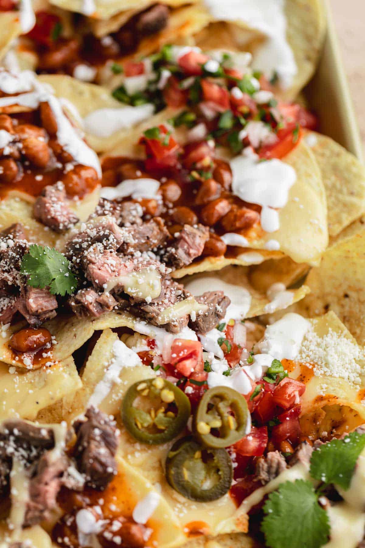 Loaded Steak Nacho Recipe topped with sour cream, salsa, jalapenos and cotija cheese. 