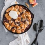 Cinnamon Roll Peach Cobbler on a plate topped with cream cheese frosting.