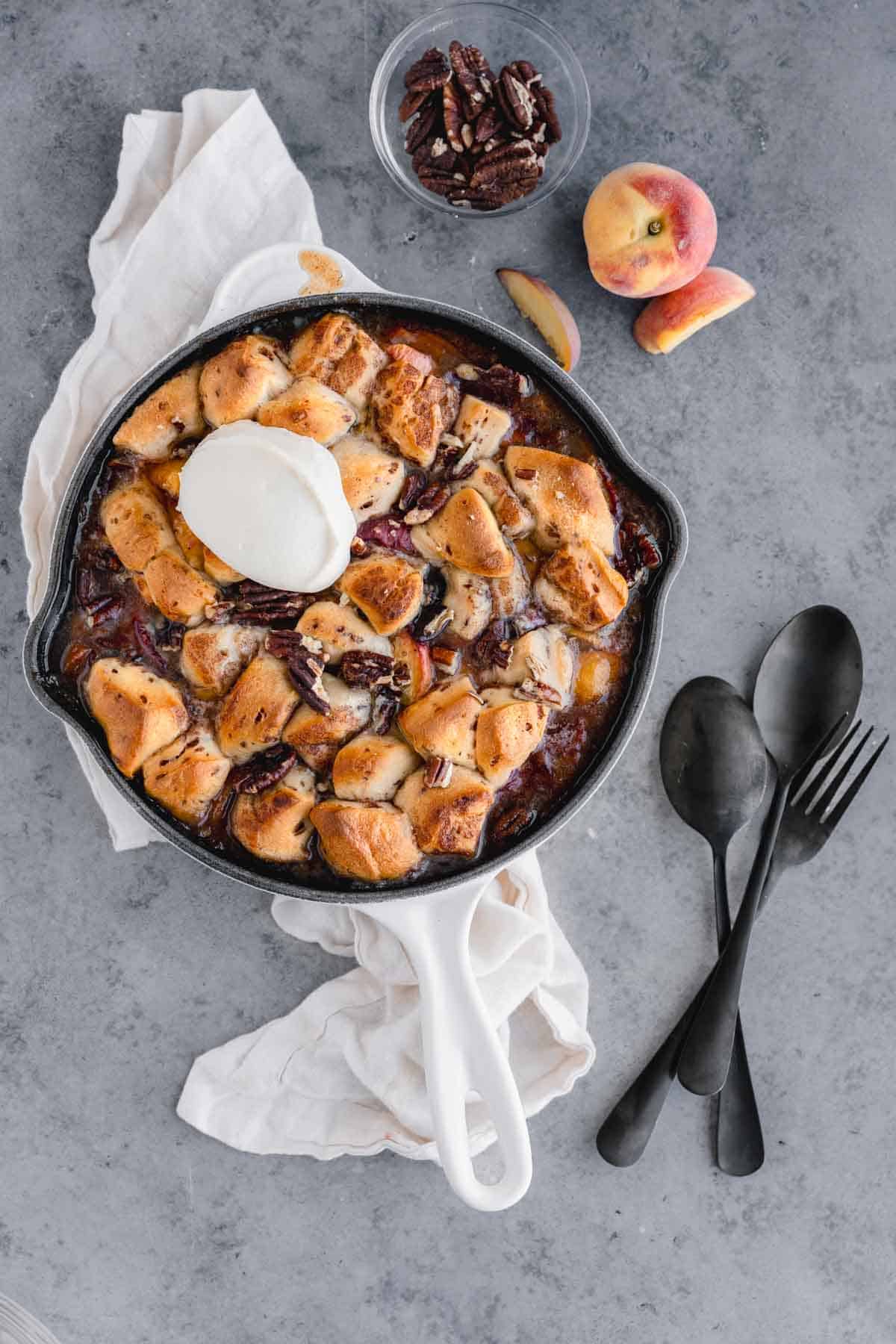 Cinnamon Roll Peach Cobbler in a skillet topped with cream cheese frosting. 
