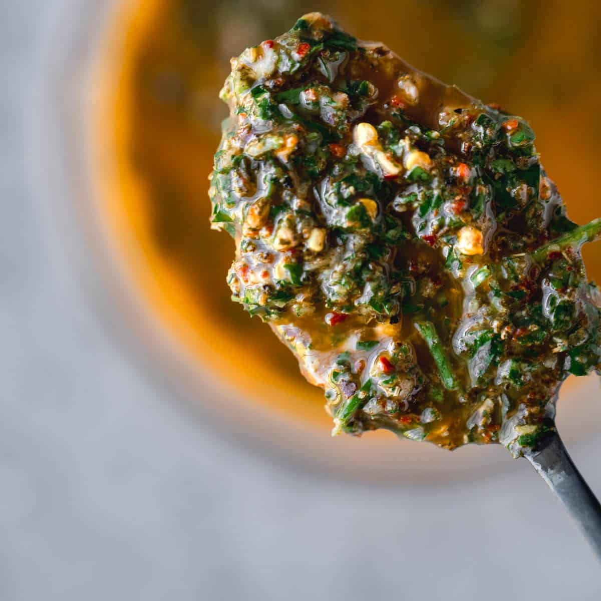 A spoonful of chimichurri over the top of a small bowl full of chimichurri.