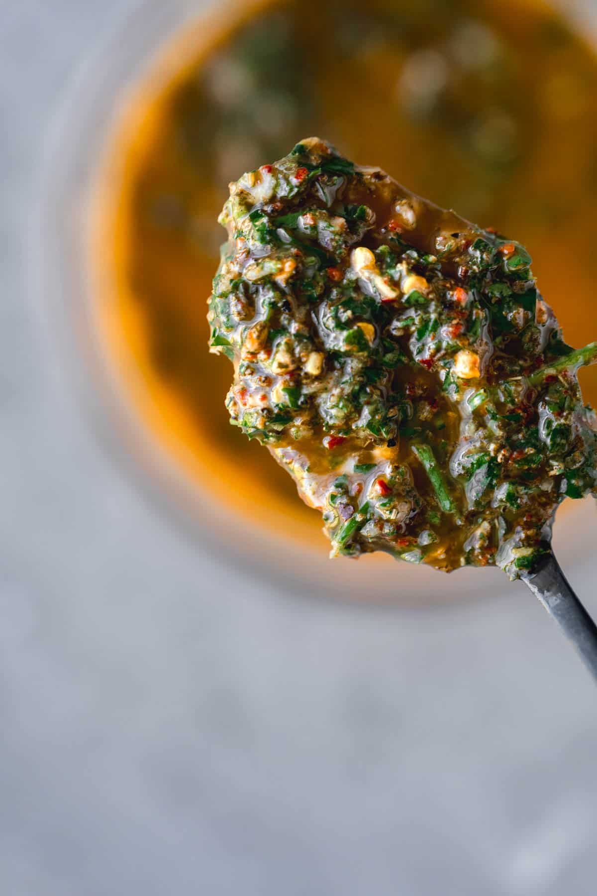 A spoonful of chimichurri over the top of a small bowl of chimichurri. 