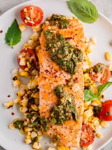 Chimichurri Salmon on a plate with roasted corn, tomatoes and basil.