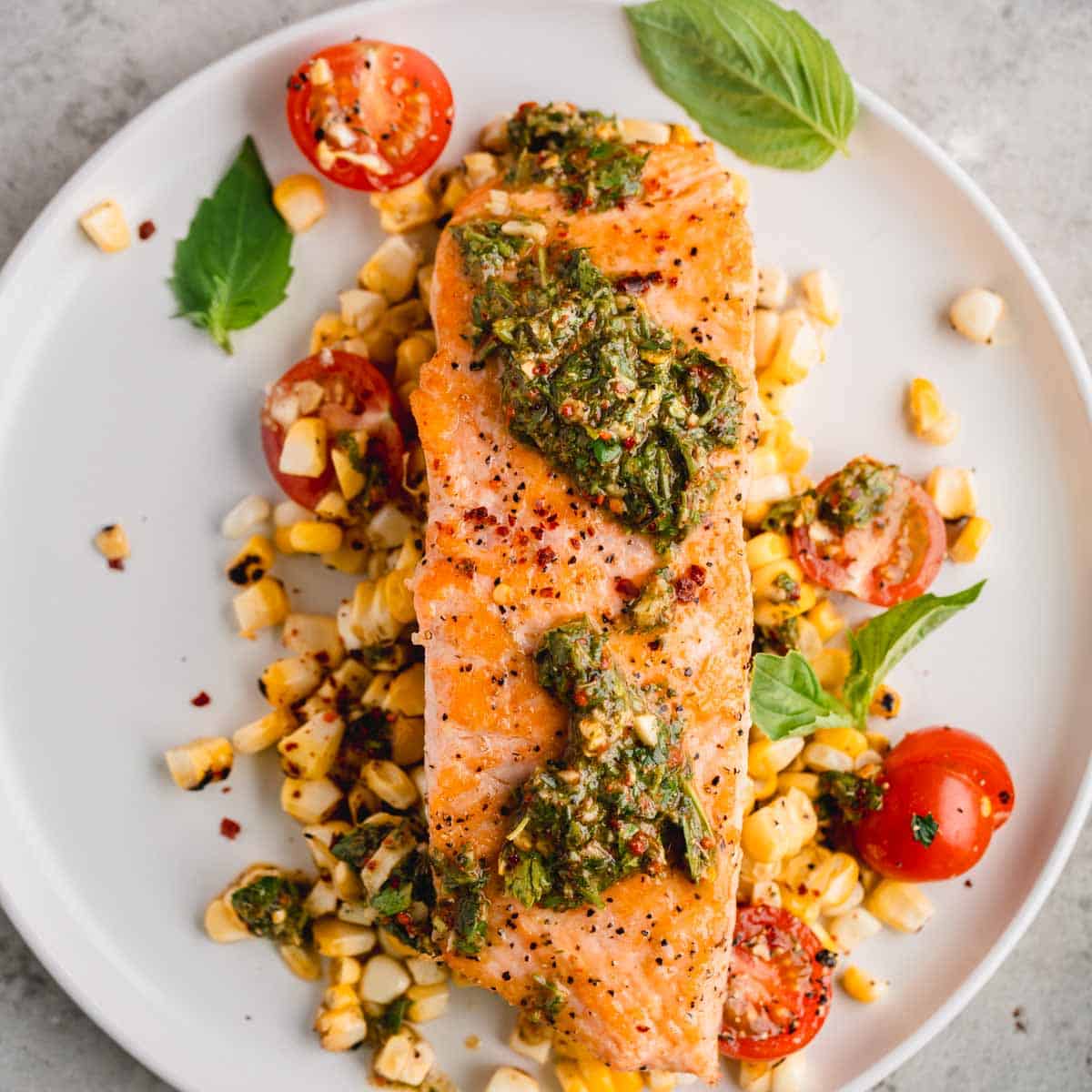 Chimichurri Salmon on a plate with roasted corn, tomatoes and basil.
