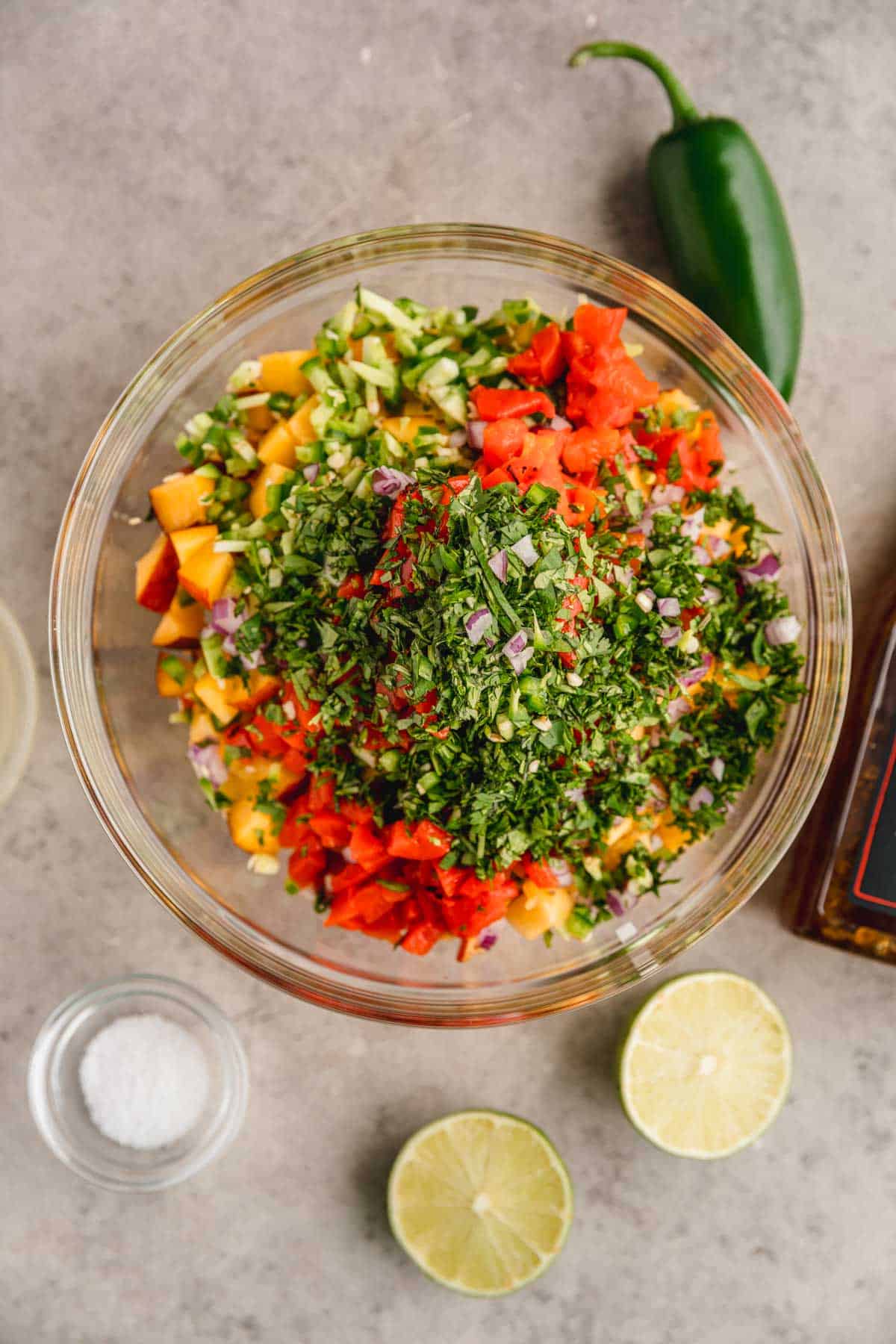 All ingredients for peach mango salsa in a bowl with salt, limes and jalapeno to the side. 