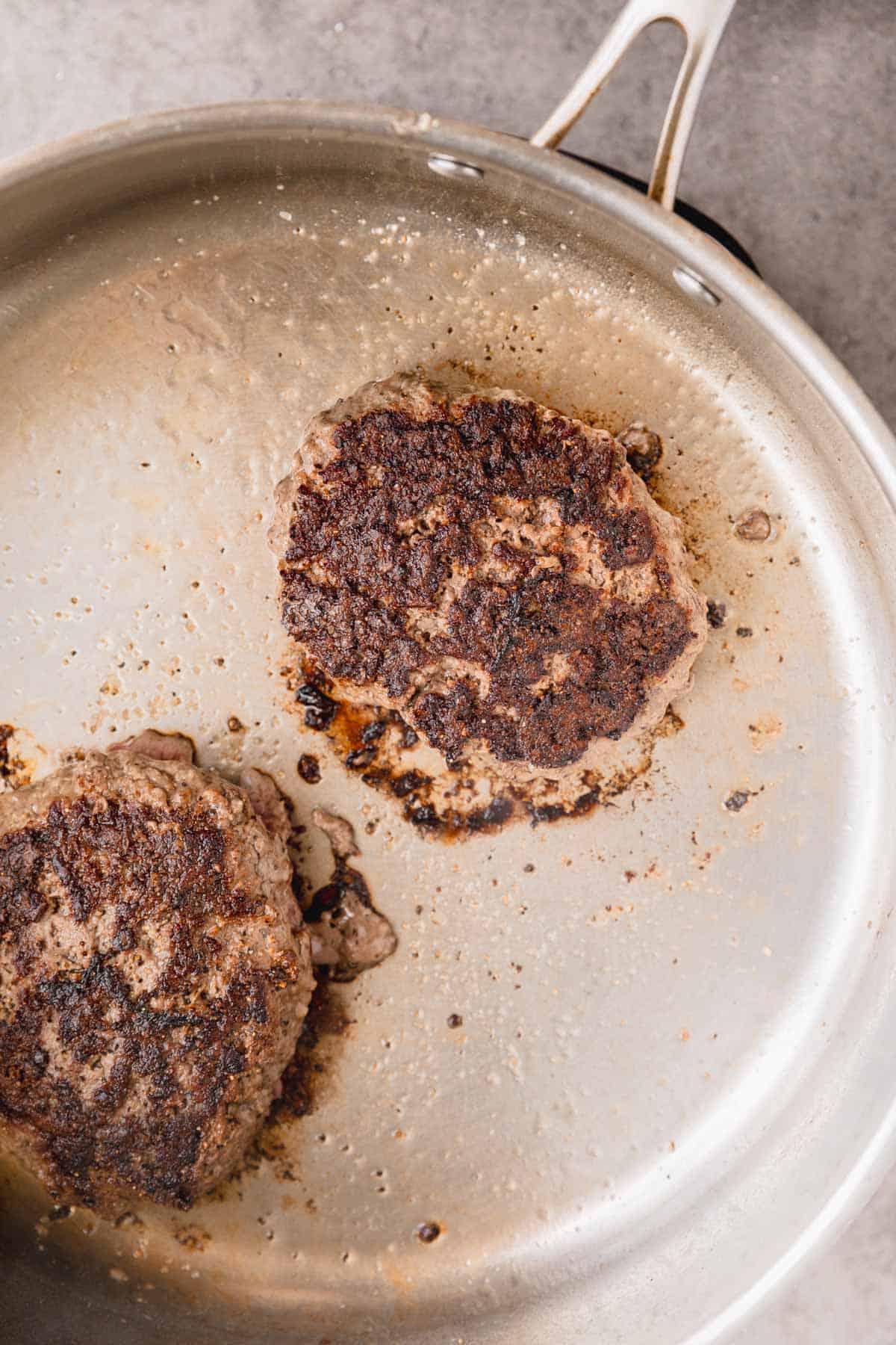 Wagyu burgers being cooked in a skillet.