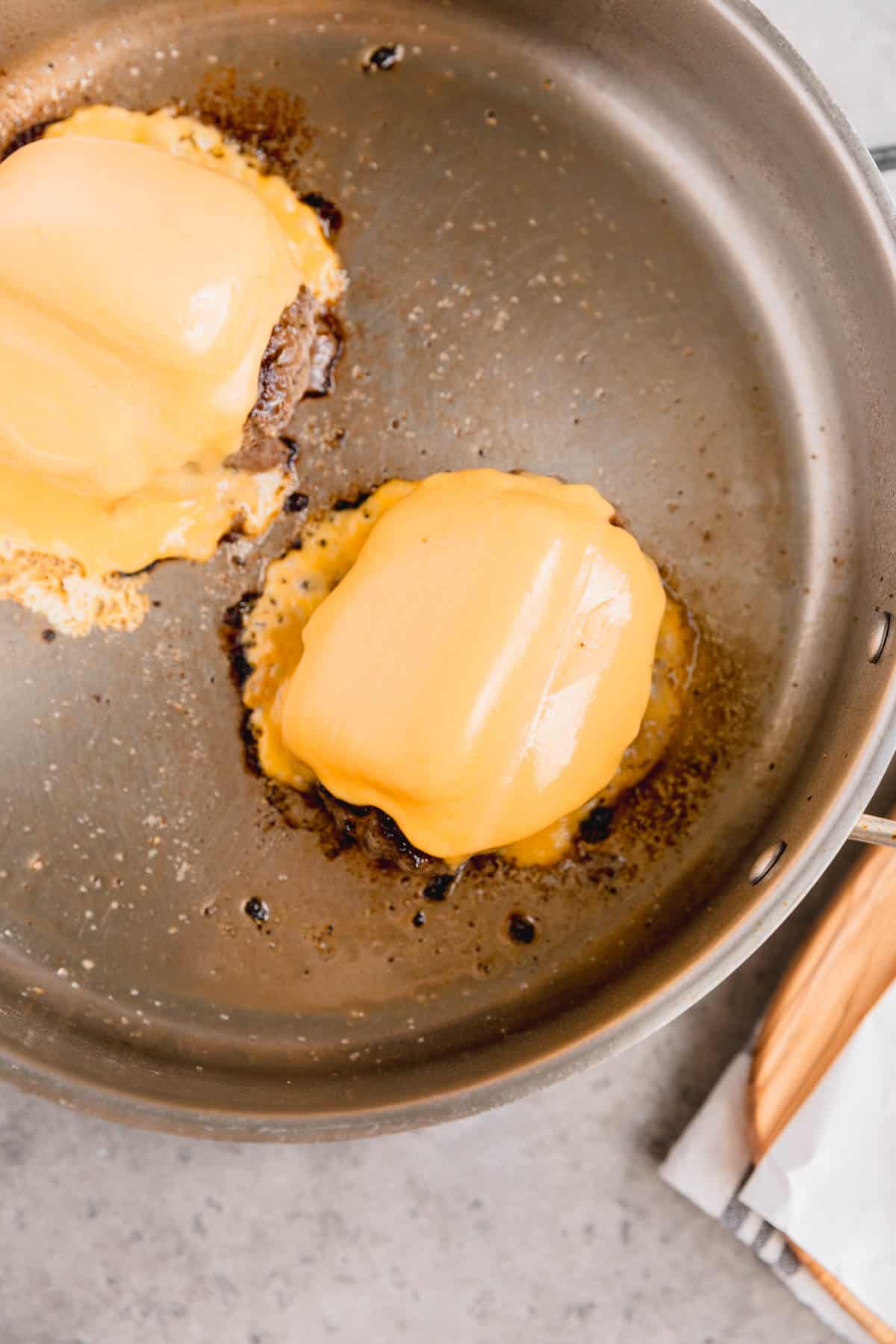 Velveeta cheese melted on top of wagyu burgers in a skillet.