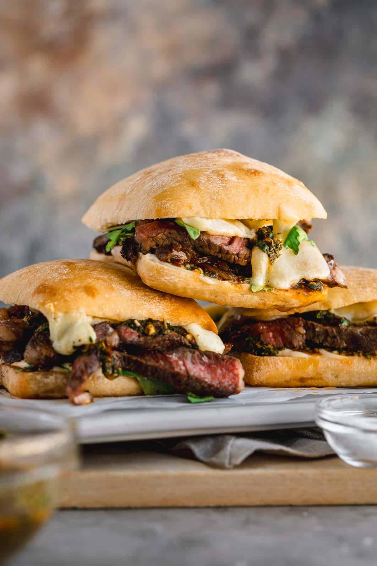 Ribeye Steak Sandwich with Chimichurri, arugula and melted cheese stacked on top of each other. 