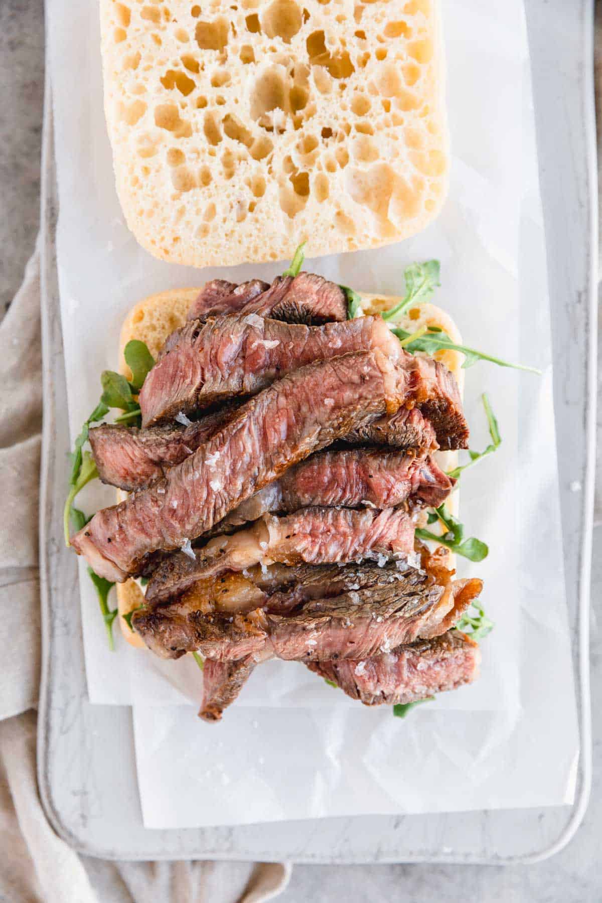 Sliced ribeye steak topped with flaky sea salt on ciabatta bread. 