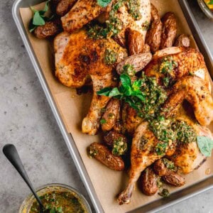 Roasted half chicken topped with chimichurri sauce on a sheet tray.