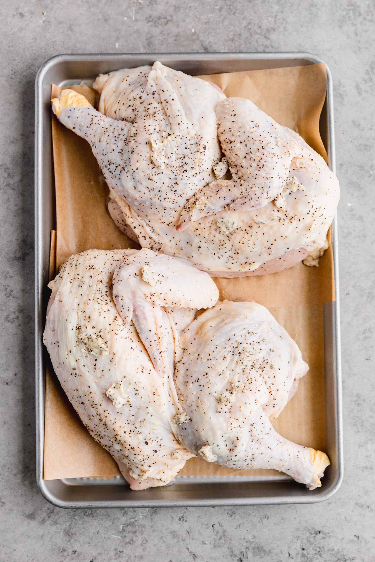 Half chicken seasoned to be roasted on a sheet tray.