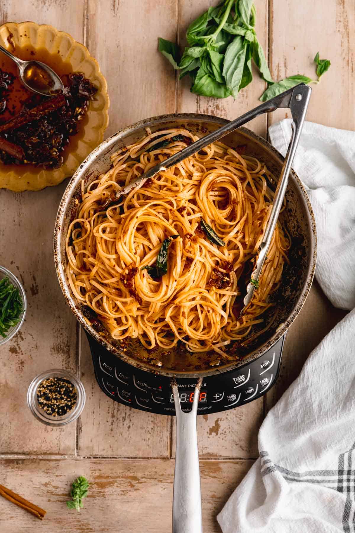 Rice noodles in chili oil in a pan with tongs. 