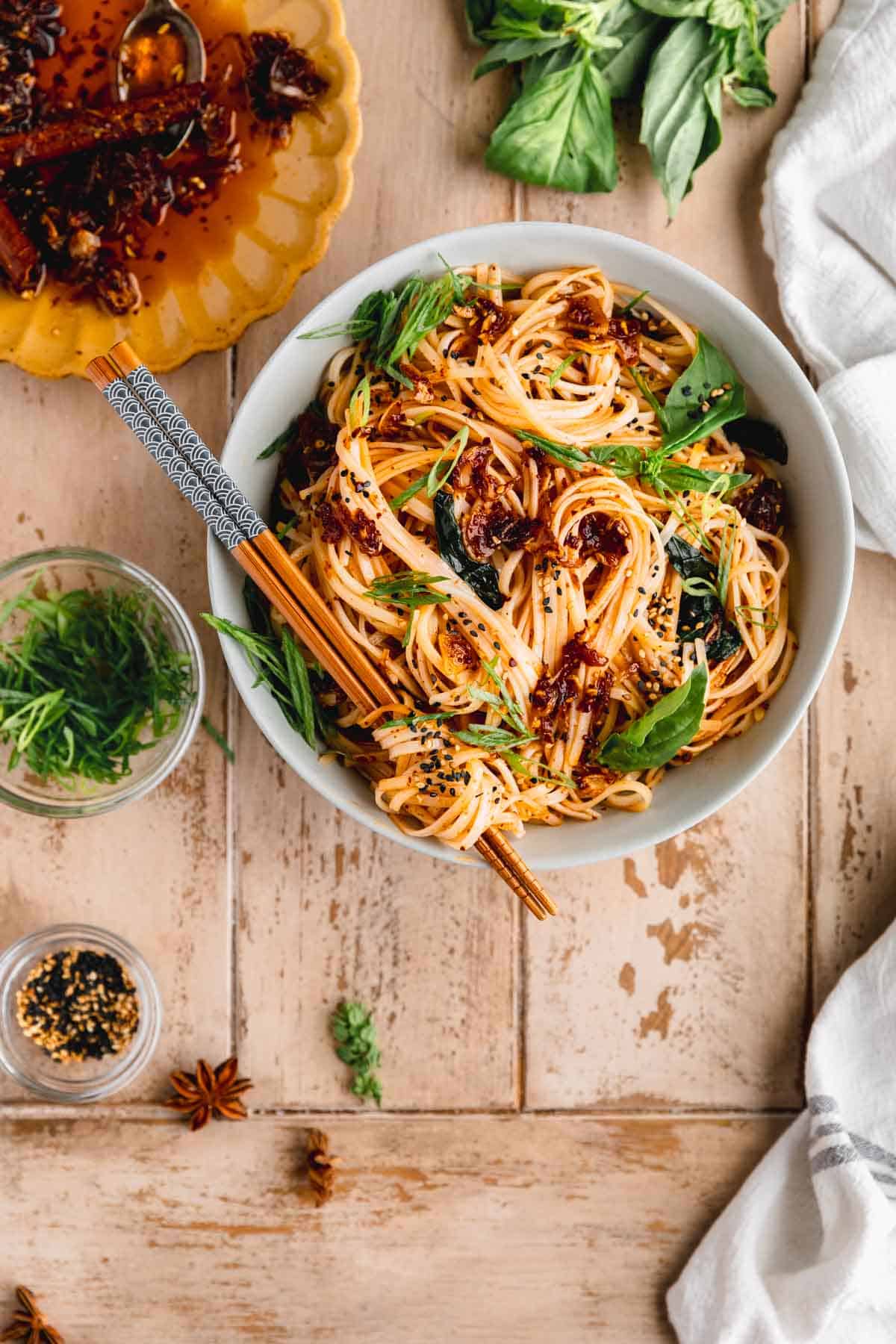 Chili Garlic Noodles in a bowl with chop sticks and herbs to the side.