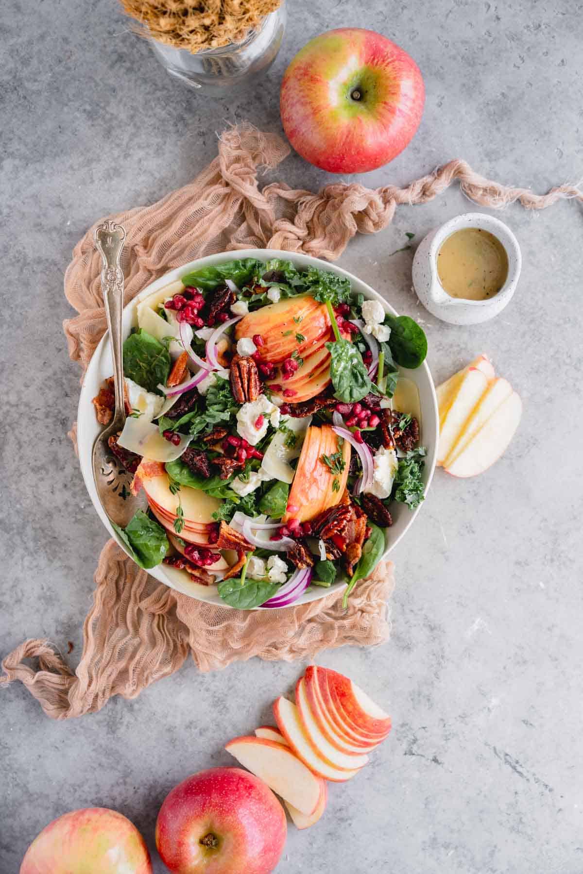 Kale Apple Salad in a bowl with sliced apples and a container of dressing on the side. 