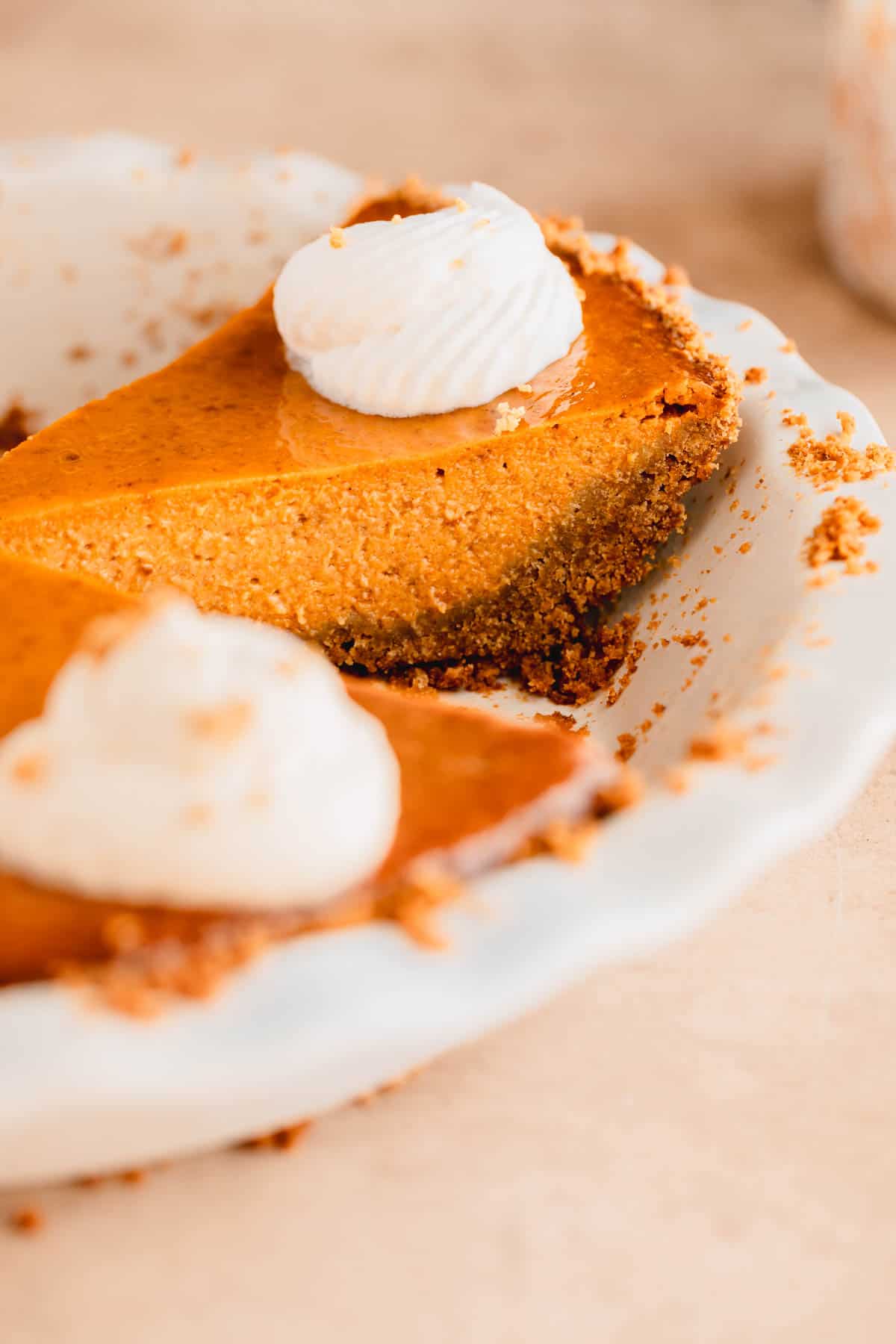 A slice of pumpkin pie with graham cracker crust in a pie pan. 