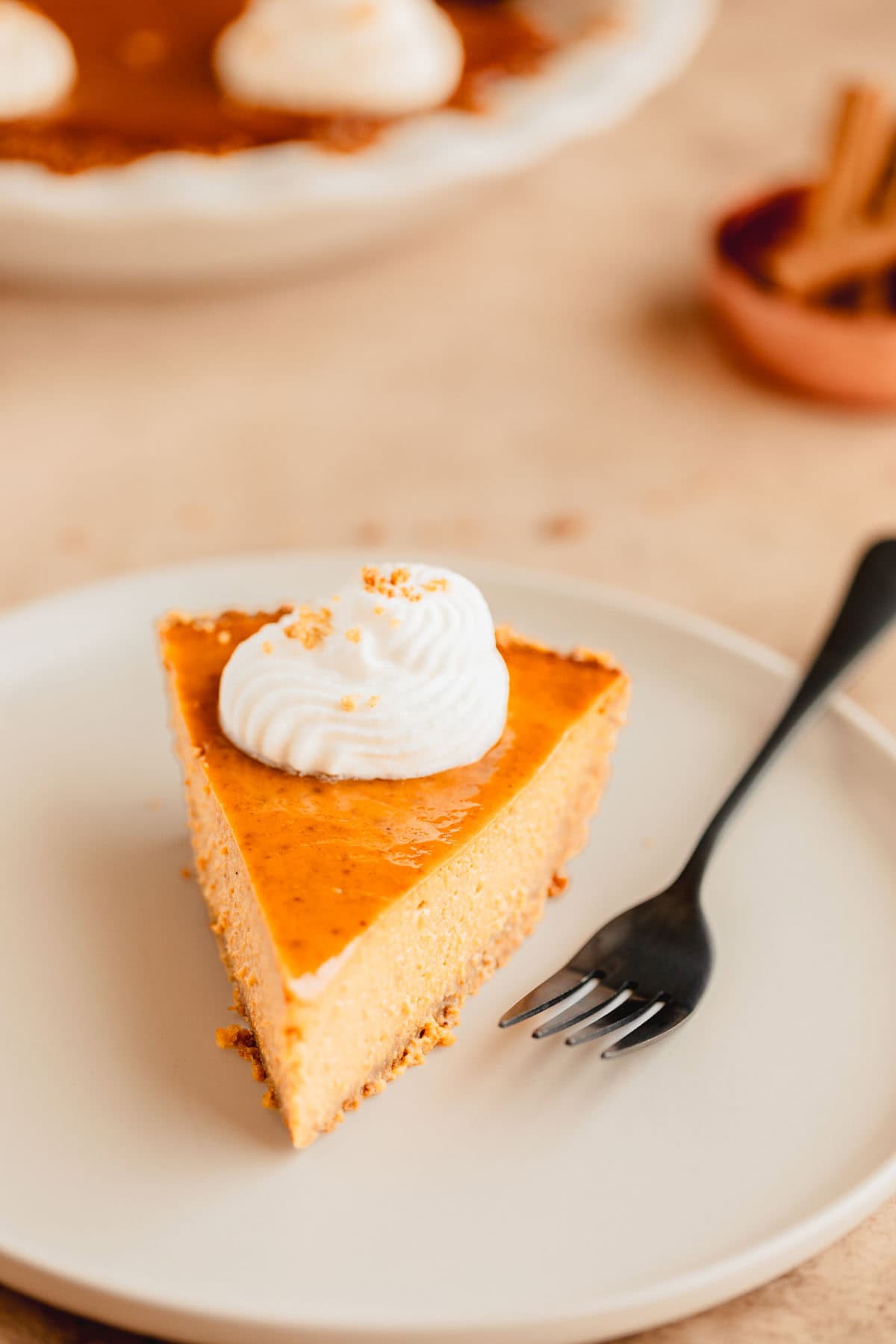 A slice of pumpkin pie with graham cracker crust on a plate with a fork. 