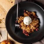 Apple Cranberry Crisp in a bowl with a scoop of vanilla ice cream and a fork.
