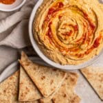 Harissa Hummus in a bowl surrounded by pita pieces.