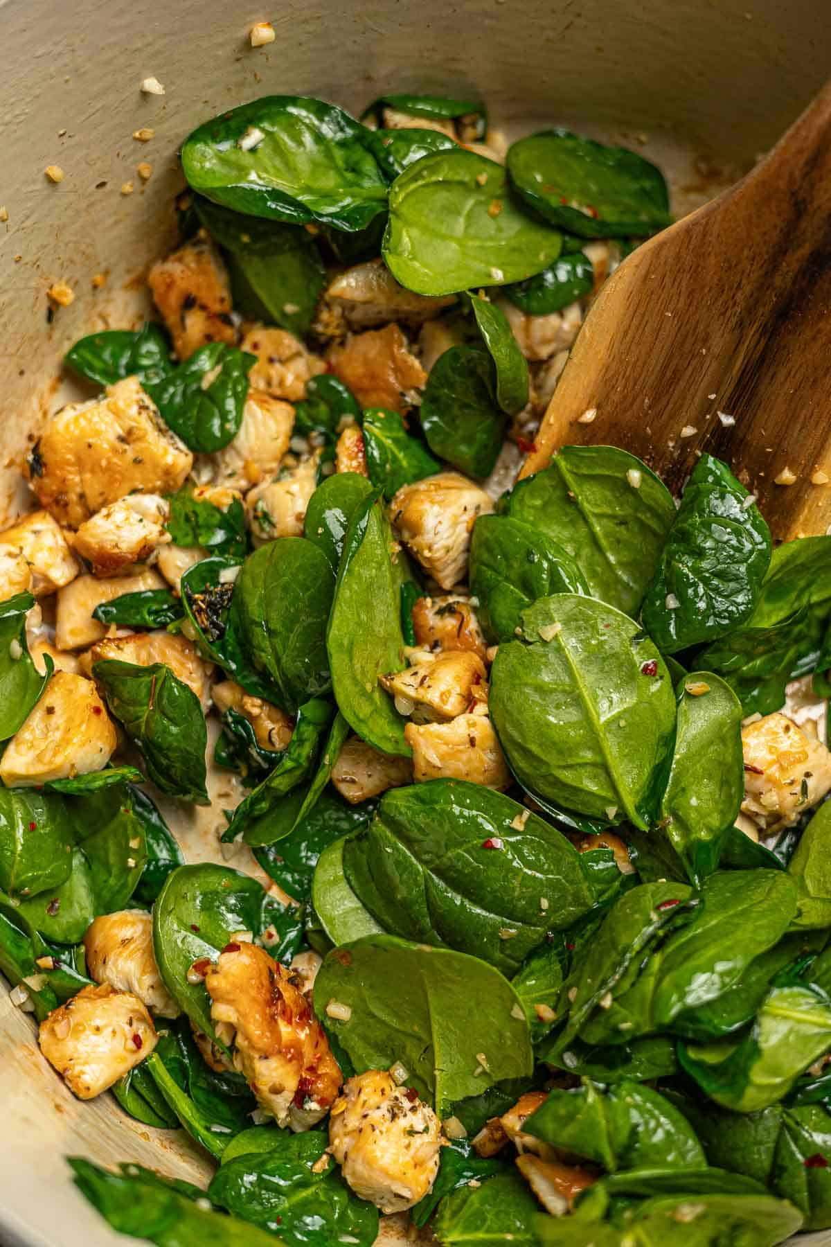Chicken in a pot with sundried tomatoes, spinach and garlic being added.