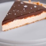 A slice of Peanut Butter Pretzel Pie with Chocolate Ganache and flaky sea salt on a stack of plates.
