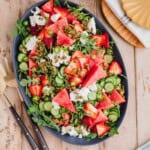 Spicy Watermelon Arugula Salad with a sweet and smoky Chipotle Strawberry Vinaigrette on a large salad platter with serving utensils aside.