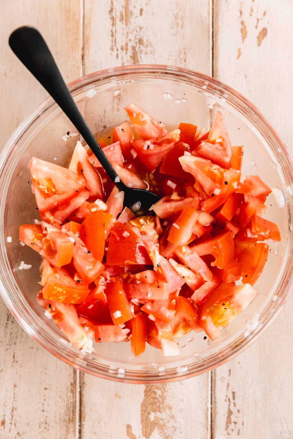 Tomatoes mixed with shallots, salt, pepper and champagne vinegar in a circular dish with a spoon.