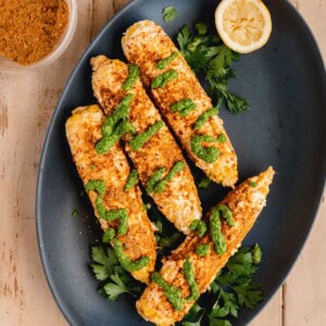 Shawarma Corn on the Cobb topped with garlic mayo, shawarma seasoning and schug sauce on a serving platter.